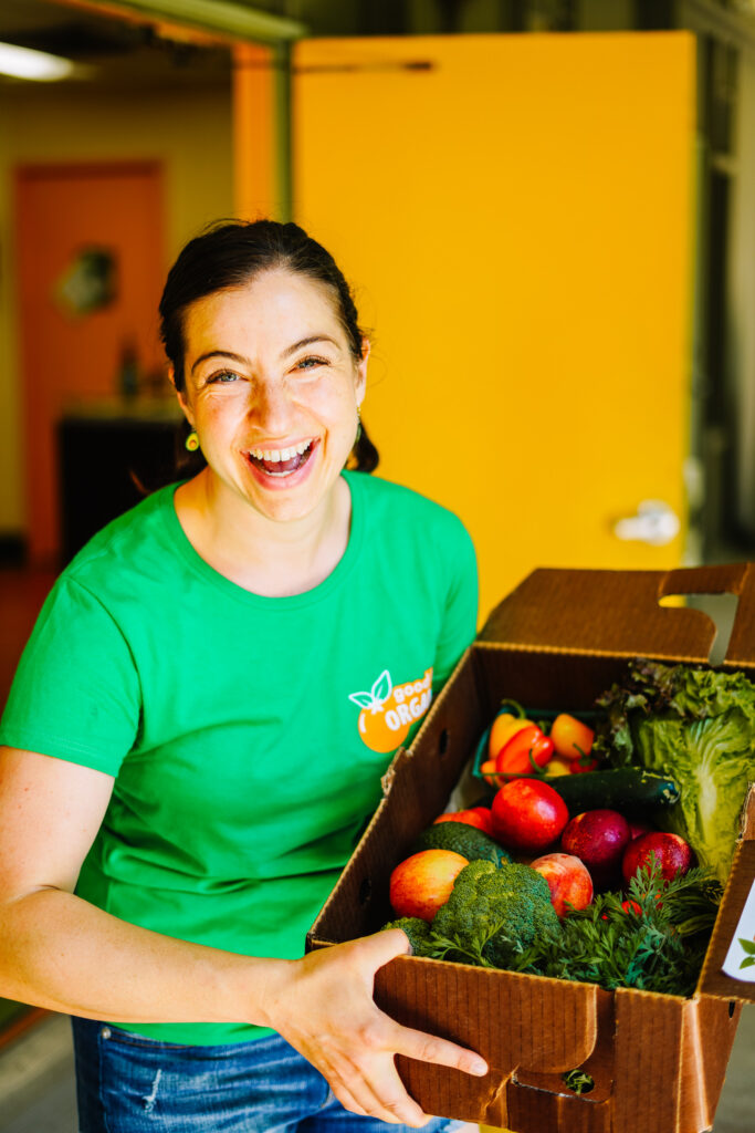 Picture of cofounder Samantha Sirota smiling and holding a half box of fruits and vegetables