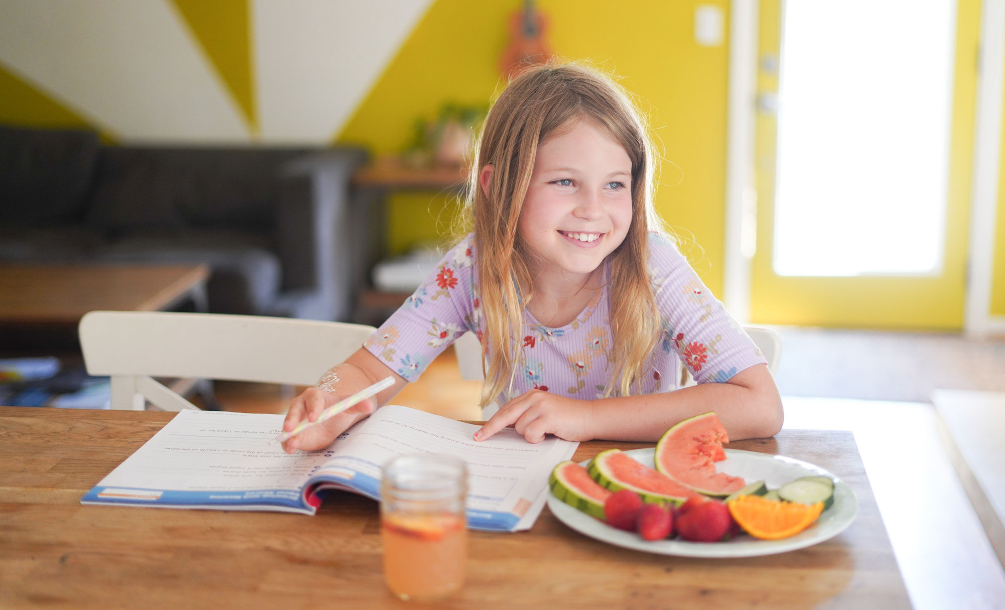 young girl doing her homework with a plate of fruit in front of her to snack on