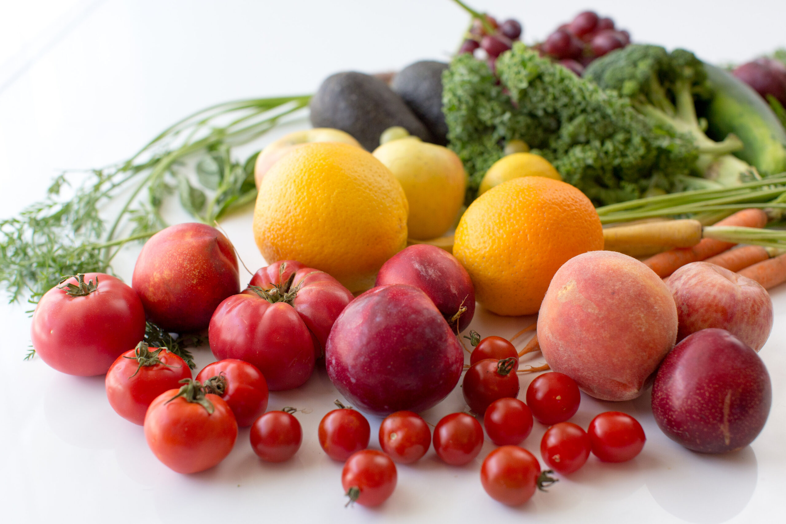 rainbow of organic fruit tomato, plum, orange , apple lemon and veggies carrots avocado kale cucumber and purple grapes